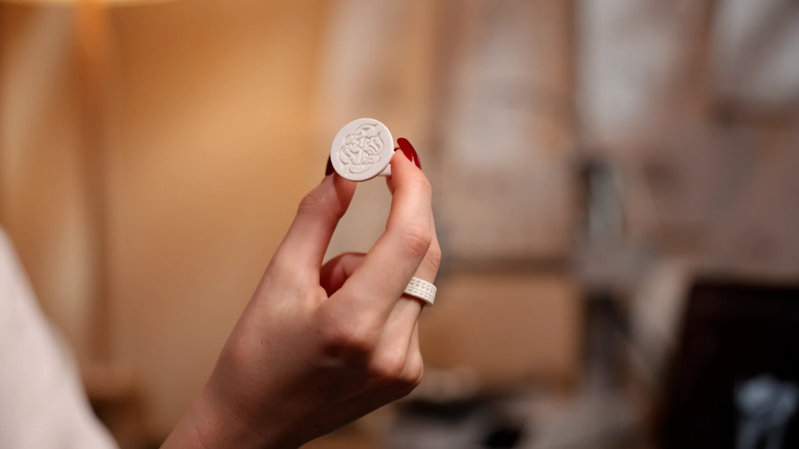 A hand holding a ring with a round top carrying a relief logo.