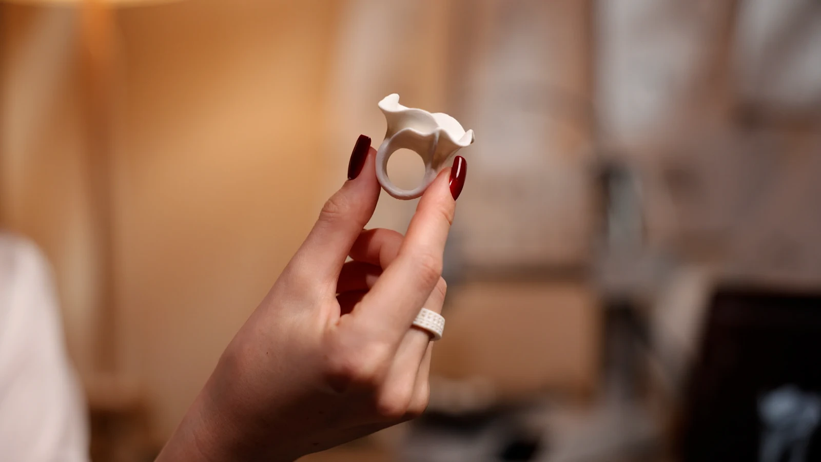A hand holding a ring with a flowing, petal-like top.